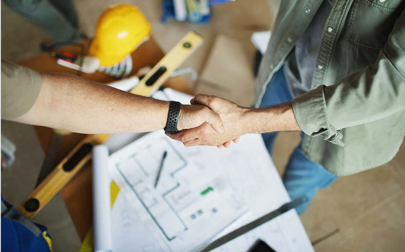 Handshake over construction plans and tools.